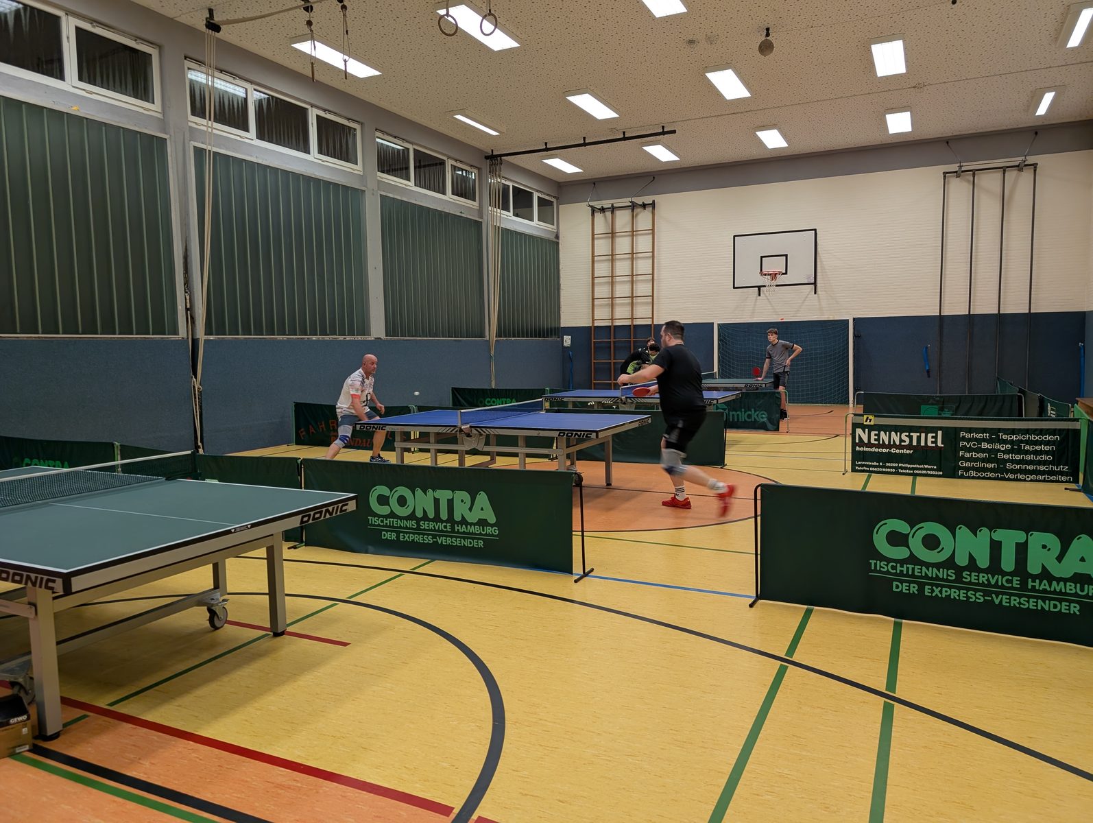 Mehrere aufgebaute Tischtennisplatten mit Spielern in der Schulturnhalle Schenklengsfeld.